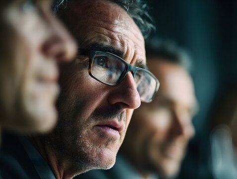 Intense close-up of a mature man wearing glasses with a focused gaze and furrowed brow reflecting deep concentration and intellectual rigor in a professional environment