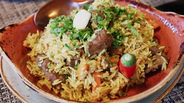 A plate of rice mixed with chunks of meat and vegetables, topped with chopped herbs and a clove of garlic