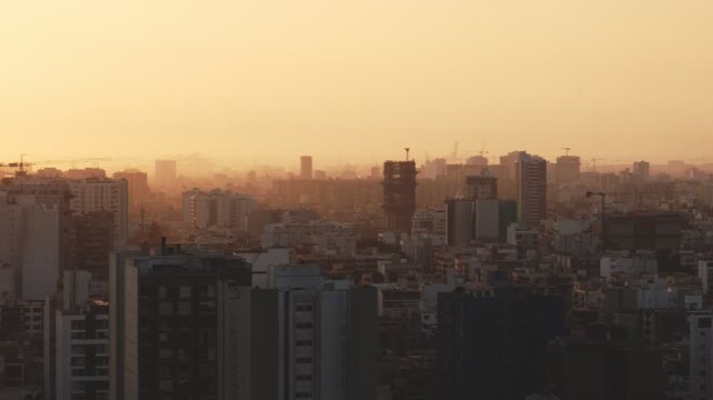 Golden sunset light illuminating the hazy city skyline of lima, peru with construction cranes