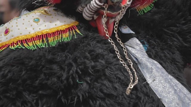 Seen up close, a bear from the Bolivian dance called Diablada dances with great energy. The bear is black, wearing a mask, horns, and colorful accessories.