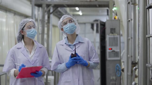 Food factory automated production line, Laboratory worker inspecting industrial equipment cleanroom factory corridor safety mask goggles glove clipboard radio quality inspection teamwork production