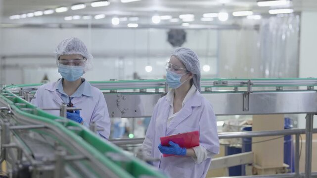 Food factory automated production line, Laboratory worker clean room inspection of production line with clipboard and radio communication, industrial quality control and safety process factory