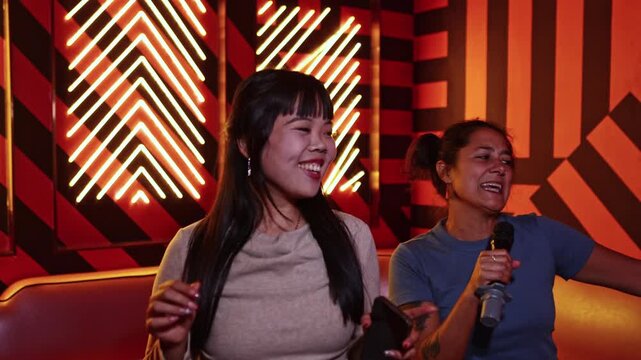 Two happy women singing karaoke together at a party