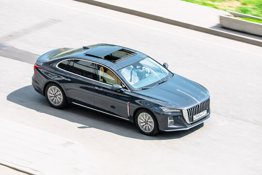 Hongqi H5 on the road in motion. Fast speed drive on city road. Above front side view of moving black car on the street