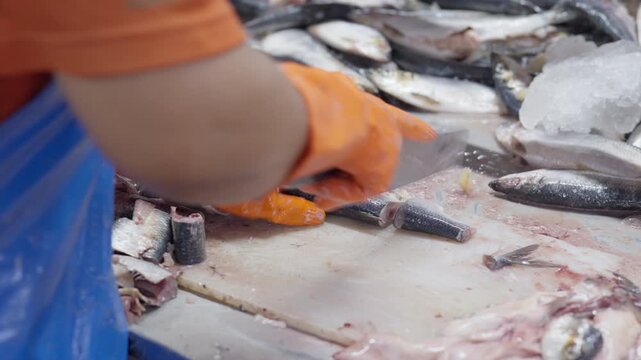 Food factory automated production line, Fresh fish market worker cleaning seafood on ice with orange glove and apron at stall, fish processing and sale display, wet market hands and knife prep