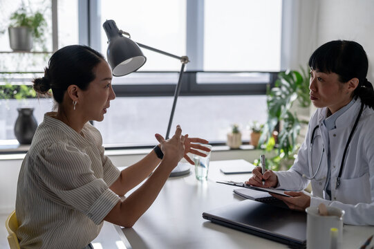 Female physician talking with patient during healthcare consultation in modern office. Medical advice, emotional support and preventive care concept.