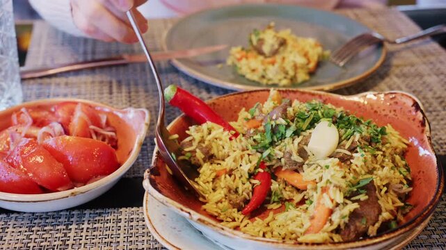 A plate of rice mixed with chunks of meat and vegetables, topped with chopped herbs and a clove of garlic