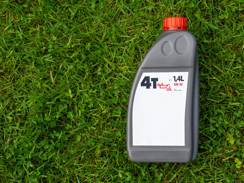 Plastic container with four-stroke engine oil SAE 30 lying on fresh green grass. Blank white label mockup on motor oil bottle with copy space for branding and advertising