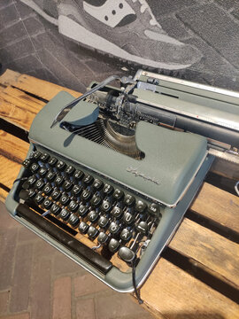 Bremen, Germany - May 09, 2026: Vintage Olivetti typewriter with black keys and silver accents displayed on wooden pallets against a textured wall background