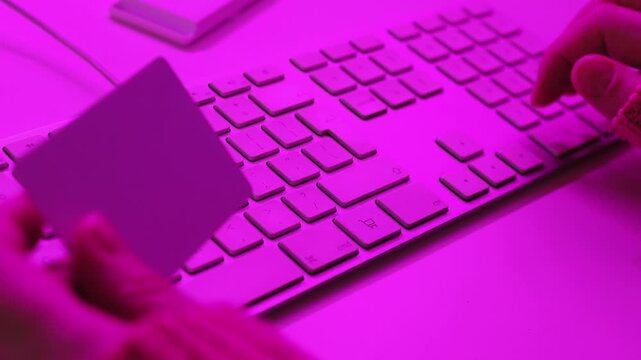 Close-up of a woman's hands typing on a keyboard while holding a credit card for an online purchase