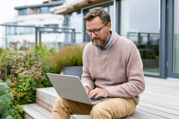 Fototapeta premium Landscape designer using laptop outdoors near modern terrace project, Scandinavian style.