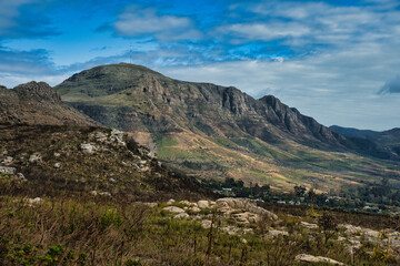 Fototapeta premium A panoramic view of a mountain range featuring rocky terrain and patches of greenery under a partly cloudy sky.