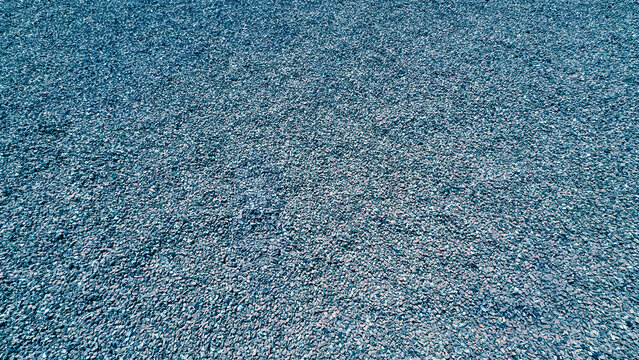 Gray Crushed Stone Texture. A high-angle, full-frame shot of a dense bed of small gray gravel and crushed stones, creating a uniform mineral texture for architectural or background use.