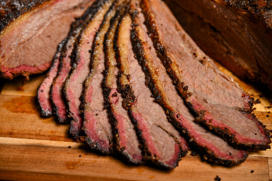 A detailed close-up shot of perfectly sliced smoked beef brisket displaying a prominent pink smoke ring, juicy texture, and seasoned dark bark on a wooden cutting board.