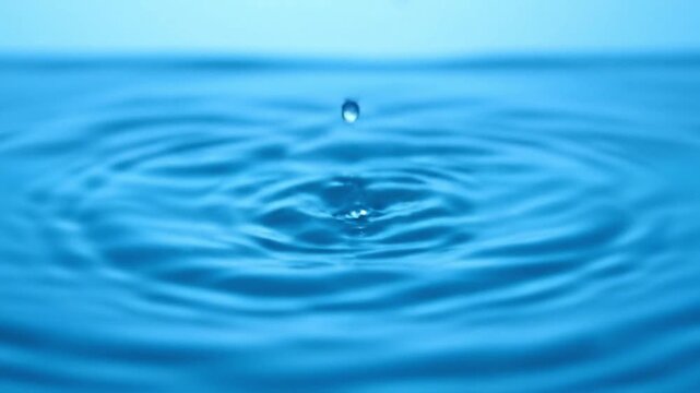 A single, crystal-clear water droplet creates beautiful, concentric ripples across a vibrant blue surface, capturing a fleeting moment of pure natural serenity and dynamic liquid motion