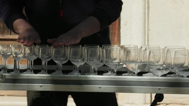 Close up of a street musician playing a glass harp. The performer's hands tap and rub the wet rims of crystal wine glasses filled with water to create acoustic music outdoors in Venice, Italy.