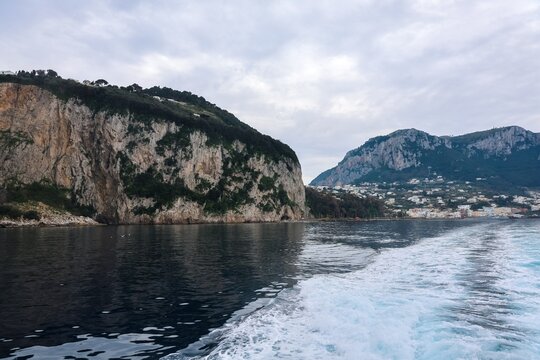 Navigating along Capri coastline with towering cliffs and town