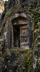 Fototapeta premium Ancient wooden door built inside a dark mysterious stone rock cave entrance