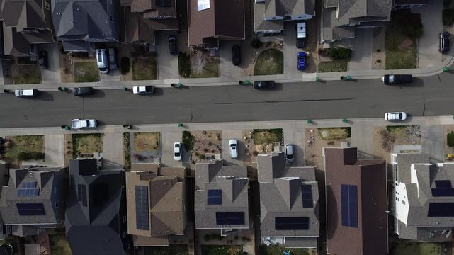 Residential arc curves through terrain edge neighborhood below North Table Mountain where solar equipped homes contribute to clean energy. Dark roofs, winter lawns define textures in Golden, CO