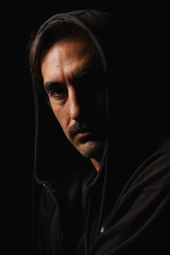 Mysterious figure in dark hoodie gazes with intensity in shadowy setting