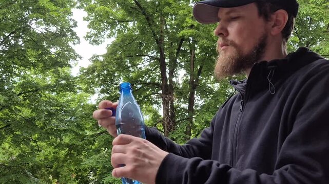 Outdoor man drinking water from plastic bottle in green nature relaxing hydration lifestyle scene