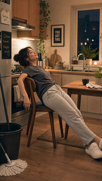 Tired young woman leaning back on kitchen chair taking a physical break after domestic chores