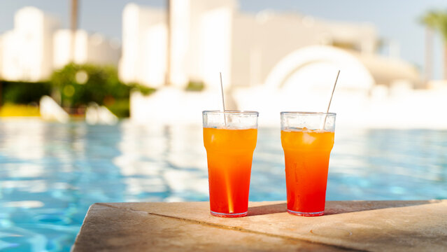 Two vibrant cocktails sit by a sunlit poolside
