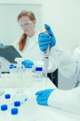 Fototapeta premium Hand wearing blue glove using an automatic pipette to transfer liquid in a modern medical research laboratory with glassware