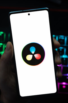 Punta Arenas, Chile &ndash; May 18, 2026: A person holding a smartphone that displays the DaVinci Resolve video editing software logo on its screen, with a blurry multi-colored backlit keyboard 