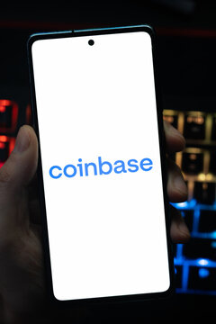 Punta Arenas, Chile &ndash; May 18, 2026: A person holding a smartphone that displays the Coinbase cryptocurrency exchange logo on its screen, with a blurry multi-colored backlit keyboard in the background