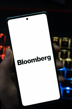 Punta Arenas, Chile &ndash; May 18, 2026: A person holding a smartphone that displays the Bloomberg financial news and media company logo on its screen, with a blurry multi-colored backlit keyboard 