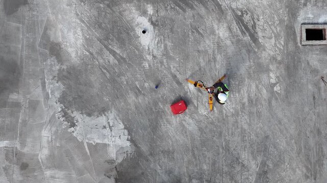 Workers in bright gear on gritty concrete surface. Red and green vests stand out against gray backdrop. Top-down view emphasizes isolation and effort. Solemn focus on task amid unfinished terrain