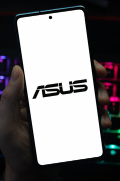 Punta Arenas, Chile &ndash; May 18, 2026: A person holding a smartphone that displays the ASUS consumer electronics company logo on its screen, with a blurry multi-colored backlit keyboard in the background
