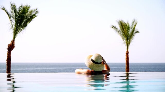Person rests in infinity pool. Palm trees frame the serene view. Ocean stretches to horizon. Sunlight glistens on calm water. Relaxation evokes tropical escape. Ideal for vacation, wellness