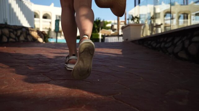 Sunlit path, feet moving forward. Legs in motion, casual stride captured. Warm tones, Mediterranean vibe. Tennis shoes, comfort, leisure. Good for travel, vacation, urban walk