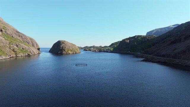 Breathtaking aerial view flying over a calm fjord towards the traditional fishing village of Nusfjord in the Lofoten Islands, Norway