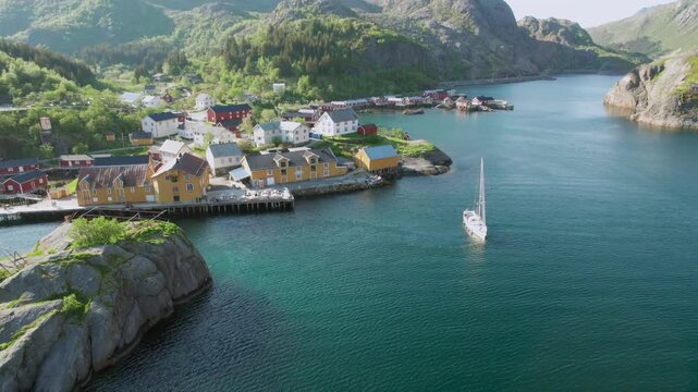 Scenic aerial view of a sailboat arriving in the traditional fishing village of Nusfjord, surrounded by majestic mountains in Norway