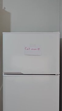 Mano colocando un cartel recordatorio con un coraz&oacute;n en la heladera