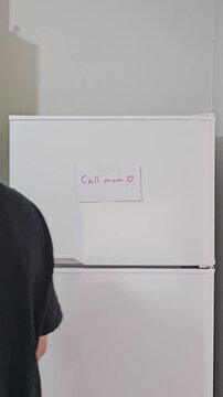 Persona de espaldas pegando una nota familiar cari&ntilde;osa en una heladera blanca