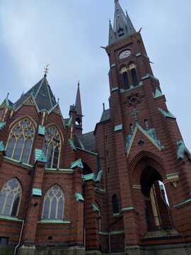 Low angle view of the historic Oscar Fredrik Church featuring red brick neogothic architecture and a tall clock tower under an overcast sky