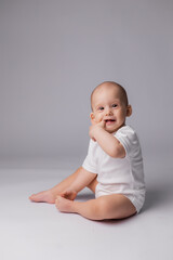 Fototapeta premium a baby in a white bodysuit is sitting on a light background in the studio