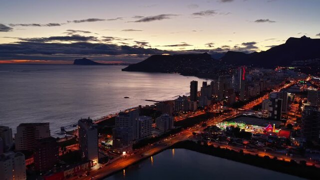 Dusk coastal skyline with illuminated boulevard and ocean soft sunset hues, calm water, glowing traffic