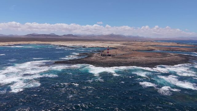 Aerial view of coastline from the Classic, candy-striped Toston lighthouse which is stands on the volcanic beach. Drone POV exploration of Fuerteventura Island. Lighthouse view.