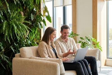 Obraz premium Smiling business colleagues looking at laptop screen in modern green office with moss wall