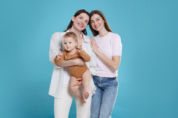 Fototapeta premium LGBT parents. Happy lesbian couple with their cute baby on light blue background
