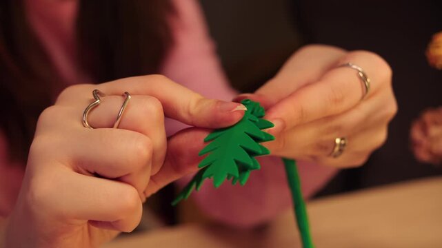 Closeup of female hands assemble flower of a construction set. Precision touch by hands of woman adding final details to floral arrangement. Attachment of a leaf to stem of a plant. Hand motor skills