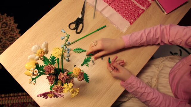 Table top view of assembling blossoms into arrangements by caucasian female hands. Meticulously designing and construction with details of constructor in home. Development of spatial imagination