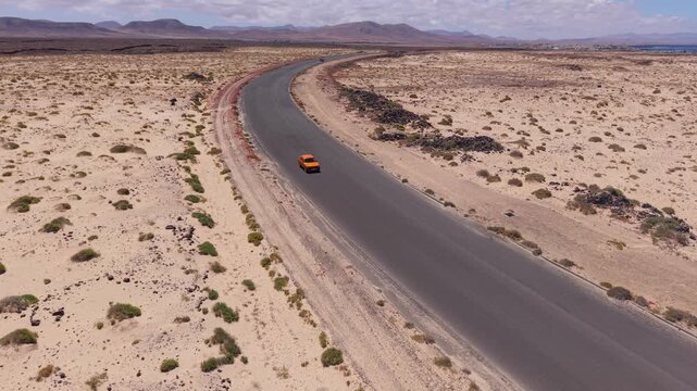 Aerial view of coastline from the Classic, candy-striped Toston lighthouse which is stands on the volcanic beach. Drone POV exploration of Fuerteventura Island. Road view with the moving cars.