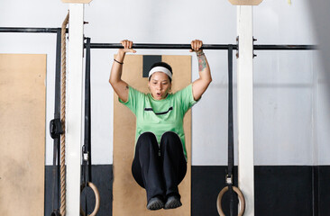 Fototapeta premium Woman exercising on pull up bar, training strength and fitness in a gym with determination