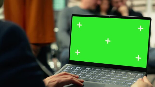 Green screen mockup with person seated inside busy bus terminal using laptop. Isolated chroma key on pc surrounded by commuters and urban transit activity, metropolitan public transportation.